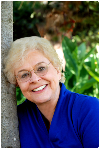 A woman with glasses leaning against a tree.