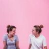 Two women sitting next to each other in front of a pink wall.
