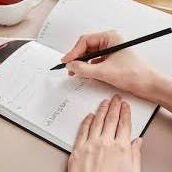 A person writing in a notebook with a pen.