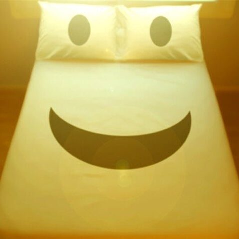 A bed with two pillows and a smiley face on it.